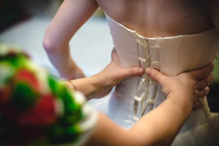 Hands of helper who helps bride to dress white wedding dress for wedding dayの写真素材
