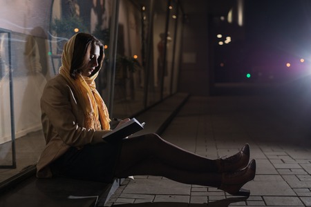 Girl brunette sitting near in the shopwindow on the night city street in a cold timeの写真素材
