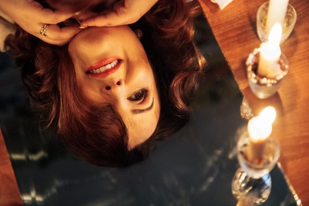 Portrait plump woman with black hair and candles in the dark room and her reflection in mirror. The...