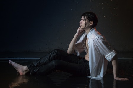 Attractive young man in white wet clothes in small pool under drops of the rain. Studio photo shootの写真素材