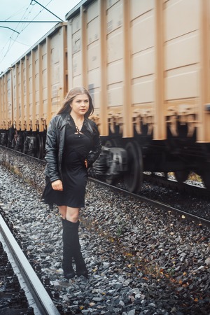 Nice girl in a black dress on a railway road near moving train