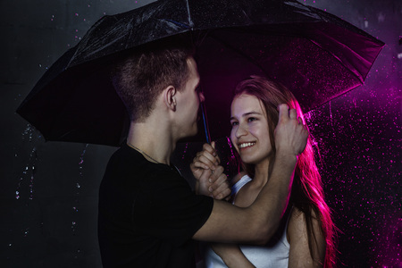 Couple young Teens stand together with black umbrella and colored light behingの写真素材