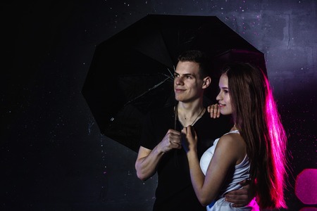 Couple young Teens stand together with black umbrella and colored light behingの写真素材