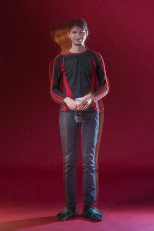 A young man in a sweater on the background of the Burgundy wall in studio with glasses in handsの写真素材
