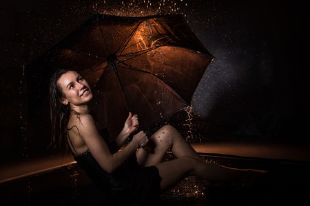 Girl in black dress with umbrella and drops of water during a photoshootの写真素材