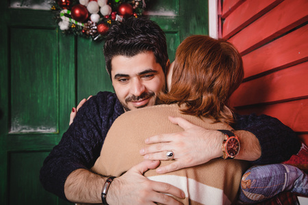 Couple consisting russian wife and turkish husband near red wall of small winter home decorated for...