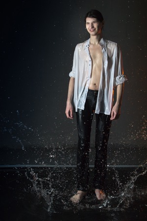 Attractive young man in white wet clothes in small pool under drops of the rain. Studio photo shootの写真素材