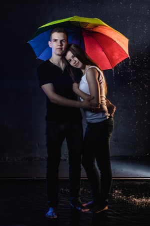 Couple young Teens stand together under rain with colored umbrellaの写真素材
