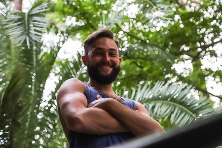 Young man with black hair and beard in the Park in a summer evening and green trees arround