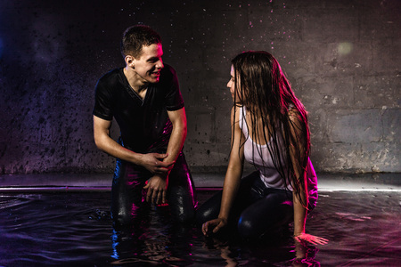 Couple young Teens together in small pool, drops of water and colored light behing them