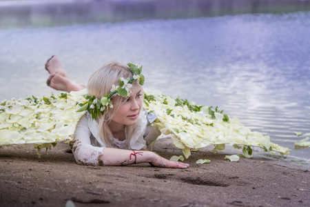 Nice blonde girl with white flower wings on the beach near river in cloudy dayの写真素材