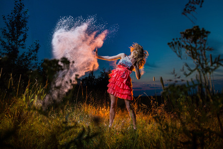 A girl in a black top and red skirt conjures up in a field and a dust cloud around. Model during a photo shoot with flour at sunsetの写真素材