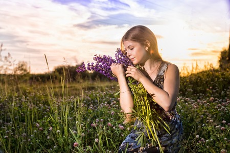 Blonde girl in a field of purple lupines in a summer eveningの写真素材