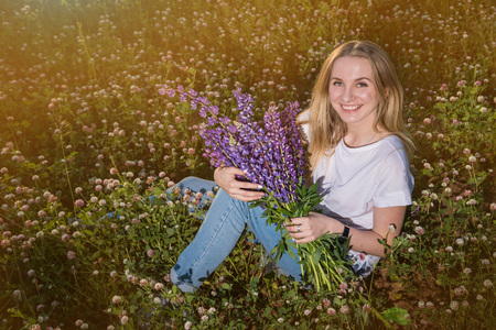 Blonde girl in a field of purple lupines in a summer eveningの写真素材