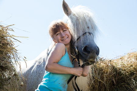 Girl with a horse near the hay on a nice Sunny summer dayの写真素材