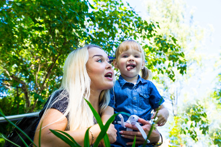 Cute blonde woman and her daughter have fun in the park. Family with happy emotion. Horizontal close up portrait little girl and her mom playing outdoor togetherの写真素材