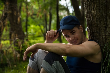 Attractive fitness man sitting near tree in a summer parkの写真素材
