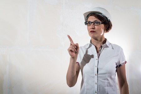 Cute nice young woman in white construction protection building helmet and unfinished apartment in the background.の写真素材