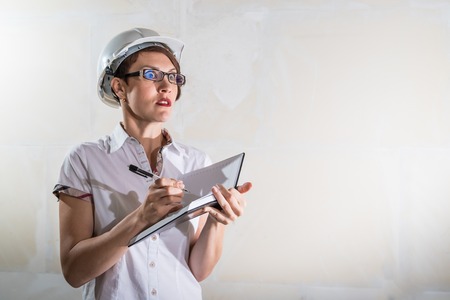 Cute nice young woman in white construction protection building helmet and unfinished apartment in the background.の写真素材