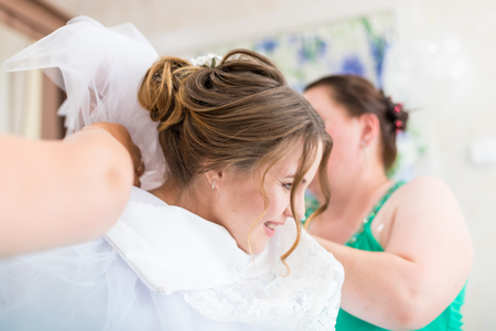 Mother helping the bride to dress her dress and tie a corsetの写真素材