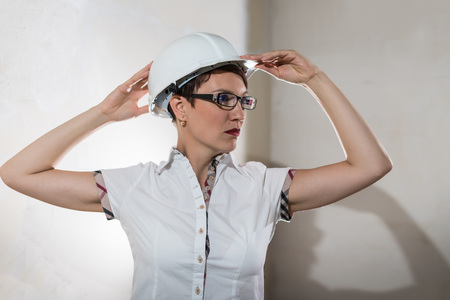 Cute nice young woman in white construction protection building helmet and unfinished apartment in the background. Female architect, desigher or engineer. New resident in an unfinished roomの写真素材