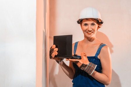 Sexy cute girl who is builder, painter, worker being in a renovated room. Laptop in hands of womanの写真素材