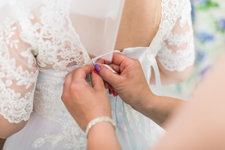 Hands of girlfriend helping the bride to dress her dress and tie a corsetの写真素材