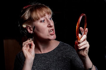 Woman with hair curlers making makeup. Girl with funny emotion on the face. Photoshoot in dark keyの写真素材