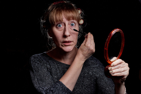 Woman with hair curlers making makeup. Girl with funny emotion on the face. Photoshoot in dark keyの写真素材