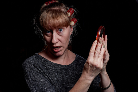 Woman with hair curlers and with funny emotion on the face. Photoshoot in dark keyの写真素材