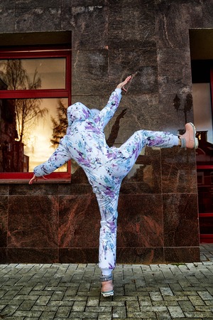 Girl in a beautiful white jumpsuit in the city having fun near red wall of building