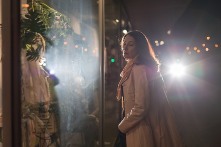 Girl brunette near in the shopwindow on the night city street in a cold time