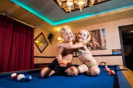 Kirov, Russia - July 18, 2018: Cute children sitting on the billiards table and balls arround....