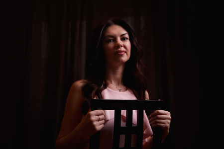 Mysterious portrait of a girl in a light dress in black room. Photo shoot in a dark keyの写真素材