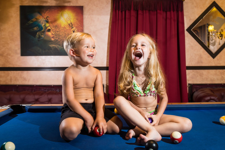 Kirov, Russia - July 18, 2018: Cute children sitting on the billiards table and balls arround. Barefoot kids. Boy and girl, brother and sister, friens have fun together during photosootの写真素材