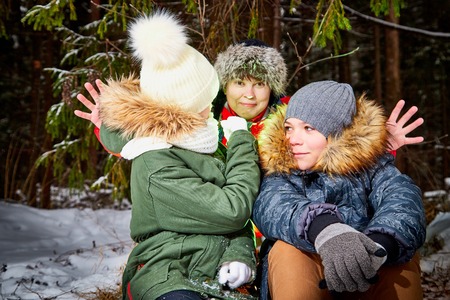 Family consisting mom, boy and girl in snow forest in a winter day. Teenagers and mother having picnic outdoorの写真素材