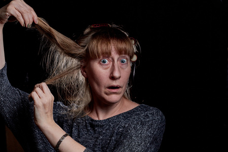 Woman with hair curlers and with funny emotion on the face. Anger, resentment, pain. Girl don't like her hair. Photoshoot in dark keyの写真素材