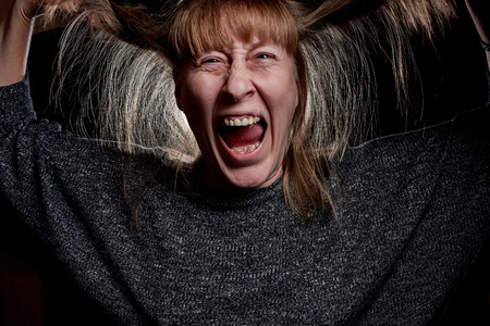 Woman with hair curlers and with funny emotion on the face. Anger, resentment, pain. Girl don't like her hair. Photoshoot in dark keyの写真素材