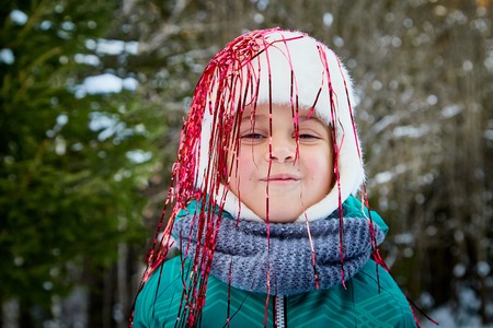 Cute small girl in tinsel in the winter forest and green trees background. New Year and Christmas conceptの写真素材