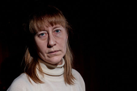 Portrait of a middle-aged sad blonde woman in the room. Photoshoot in a dark key