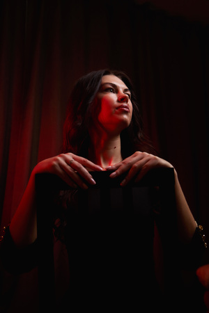 Mysterious portrait of a girl in black dress and red light background. Actress before going on stage. Photo shoot in a dark keyの写真素材