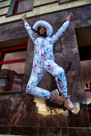 Girl in a beautiful white jumpsuit in the city having fun and jumping near red wall of building