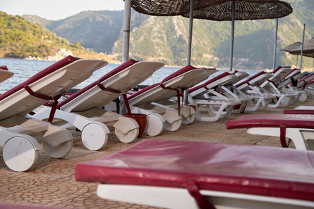 Landscape with sun beds and umbrellas in the foreground and the sea with mountains in the background in a summer dayの写真素材