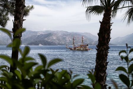 Marmaris, Turkey - May 22, 2018: Branches of trees and view of sea, mountain and ship through them. Holiday conceptのeditorial素材