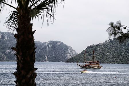 Marmaris, Turkey - May 22, 2018: Branches of trees and view of sea, mountain and ship through them. Holiday conceptのeditorial素材
