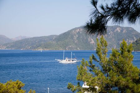 Marmaris, Turkey - May 23, 2018: Branches of trees and view of sea, mountain and ship through them. Holiday conceptのeditorial素材