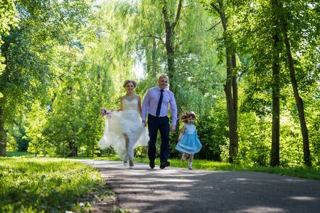 Kirov, Russia - June 29, 2018: Russian bride and groom running together with small girl in blue dress in green city parkのeditorial素材
