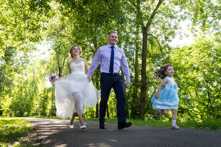 Kirov, Russia - June 29, 2018: Russian bride and groom running together with small girl in blue dress in green city parkのeditorial素材