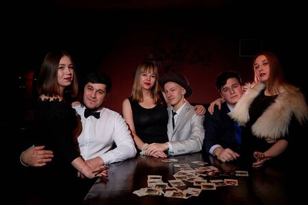 Kirov, Russia - December 19, 2018: Group of people with playing cards near table in a dark room with red light. Photo shoot in gangsters styleのeditorial素材