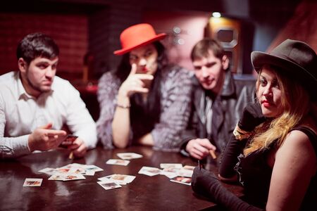 Kirov, Russia - December 19, 2018: Group of people with playing cards near table in a dark room with red light. Photo shoot in gangsters styleのeditorial素材